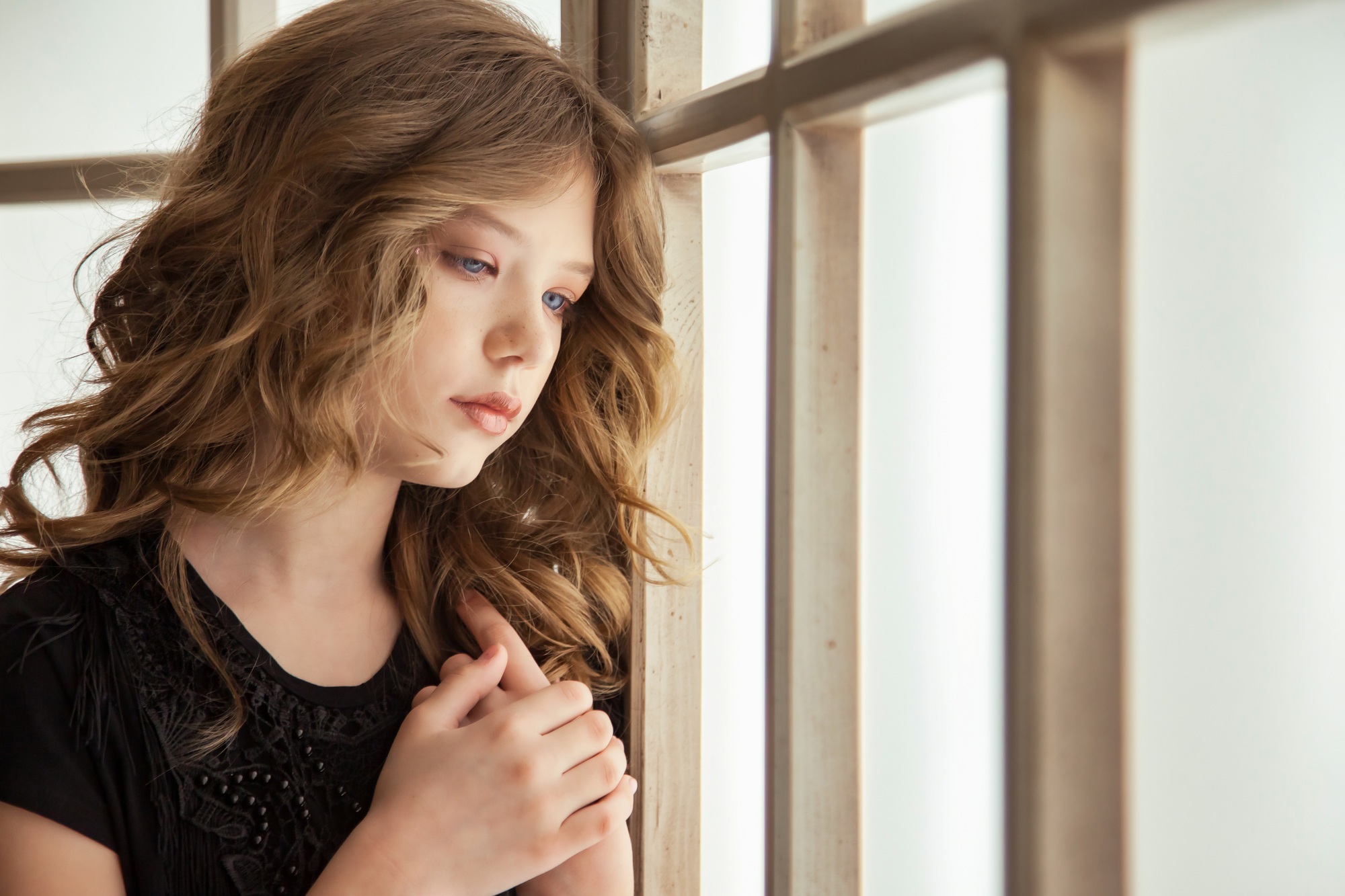 Sorrow image of teen girl in stylish black dress near large window indoors